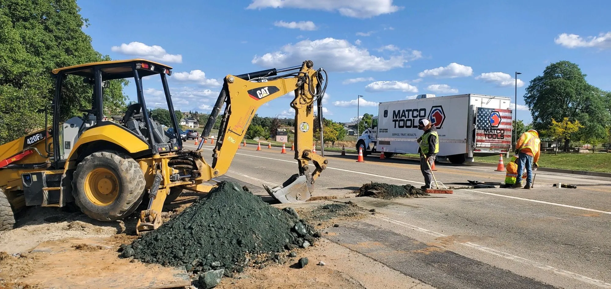 Backhoe digging along a street with Hudson Excavation crew members in safety vests nearby